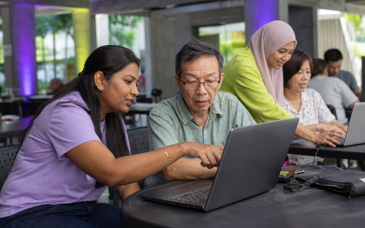 A mentor guiding an older participant through a laptop screen